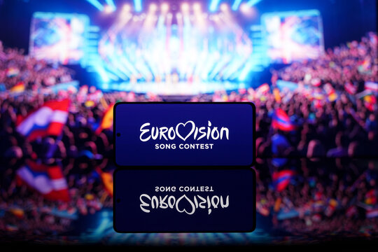 Smartphone displaying Eurovision Song Contest logo with a blurred stage and audience in the background. Music competition and entertainment concept