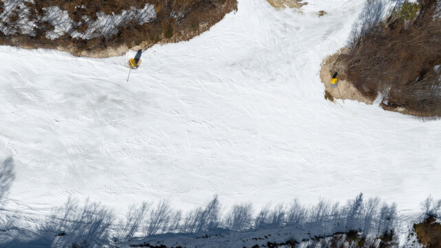 Aerial perpendicular view of an empty ski slope. It's winter, there's a lot of snow and it's a sunny day.