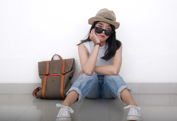 Wearing a straw hat, sunglasses, sleeveless top, and jeans, the woman sits casually on the floor. A...
