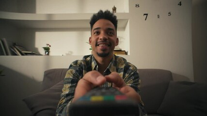 Smiling American man is sitting on couch with remote control and choosing movie.