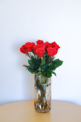 Red roses in a coffee-colored glass vase on a table, against a white background.