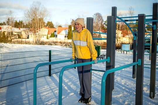 young woman in a yellow hoodie and gloves works out on parallel bars in a snowy outdoor gym