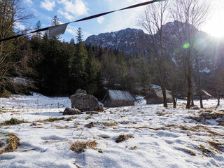Rustic Winter Cabins in Snowy Mountain Valley with Sunlight Illuminating Dramatic Peaks