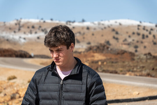 A young man in a black jacket stands before a mountain