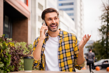 Smiling young man outdoors in casual outfit during a phone call, enjoying daylight city vibes,...