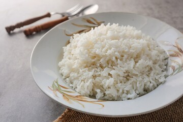 Cooked white rice or steamed rice in a ceramic plate with rice pattern screen with spoon and fork , thai jasmine rice, thai fragrant rice, 