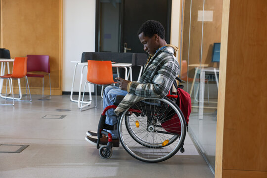 Man in wheelchair looking at smart phone in office - Powered by Adobe