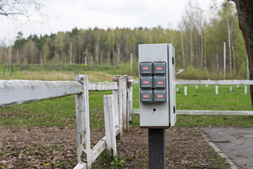 An outdoor electrical panel mounted on a metal post near a weathered wooden fence. The background...
