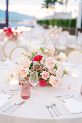 Bouquet of flowers stands on a set festive table with a lit candle