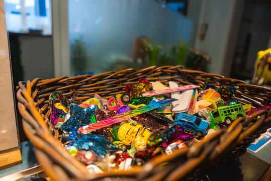 A wicker basket filled with toy cars, glittery stars, and playful items on a counter. Frosted glass panels and a person in the background suggest a hotel setting.
