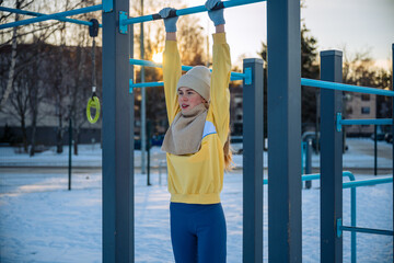 Young woman exercising on monkey bars in winter outdoor gym