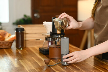 A woman is grinding coffee beans in a coffee grinder. The coffee grinder is on a wooden table.