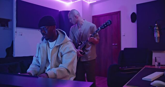 Musicians collaborate, playing keyboard and guitar, composing a new song in a modern music studio.