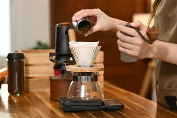A woman is grinding coffee beans in a coffee grinder. The coffee grinder is on a wooden table.