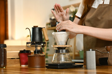 A woman is making coffee using a French press. She is pouring coffee grounds into the French press and adding water.