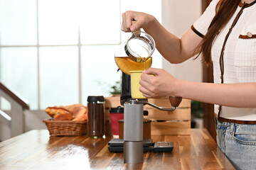 A woman is making tea in a kitchen. She is wearing an apron and holding a tea strainer.