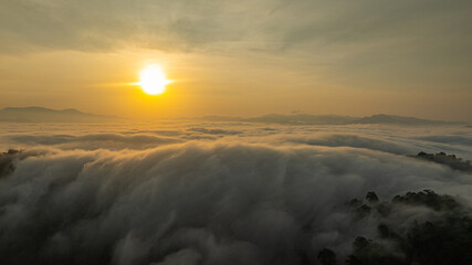 Breathtaking aerial view of the sun rising over a mountain valley covered in a dense sea of rolling...