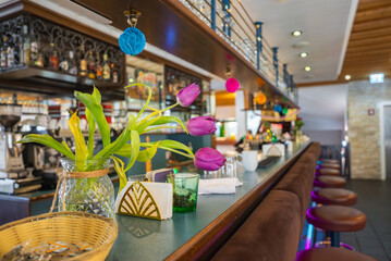 A high end bar interior featuring vibrant purple tulips, ornate shelving, cushioned stools, a polished countertop, and a warm wooden ceiling.