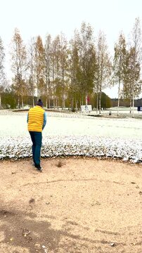 A golfer in a yellow vest and winter hat takes a bunker shot on a snow-covered golf course, aiming to escape the sand trap in cold weather.
