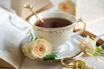 A cup of aromatic tea, a book and a rose on the table.