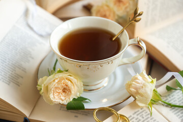 A cup of aromatic tea, a book and a rose on the table.