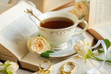 A cup of aromatic tea, a book and a rose on the table.