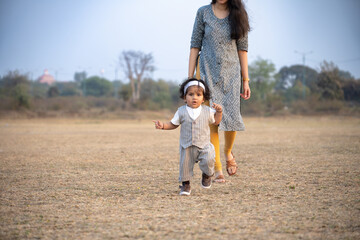 Fototapeta premium First Steps. Adorable smiling Indian mother walks with her infant son 