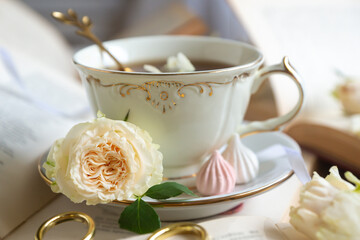 A cup of aromatic tea, a book and a rose on the table.