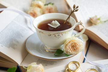 A cup of aromatic tea, a book and a rose on the table.