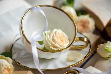A cup of aromatic tea, a book and a rose on the table.
