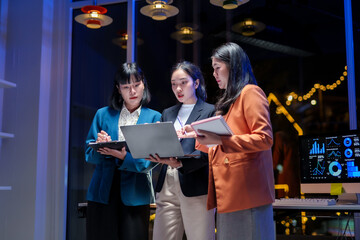 Asian businesswomen team analyzing financial data on laptop screen, working late together to discuss marketing strategy in office