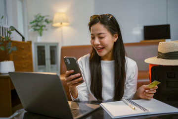 Asian woman holding credit card using smartphone and laptop for online shopping while planning vacation trip at home © Crystal