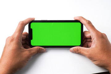 Someone hand is holding a smartphone with blank green screen display for mock up, isolated on white background. Social media scrolling, gaming and mobile apps concept