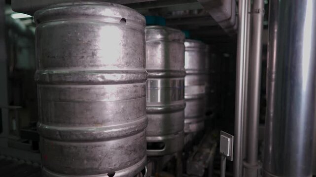 Metal beer kegs move along an automated conveyor system at a brewery for cleaning and filling. The high-tech production process ensures proper sanitization and preparation before beer is dispensed int