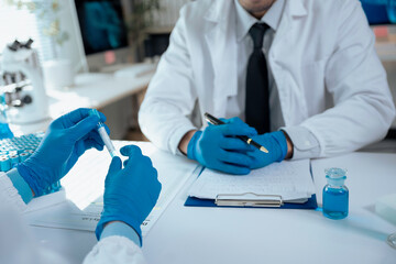 Two scientists wearing lab coats and gloves examining test tube with blue liquid in laboratory,...