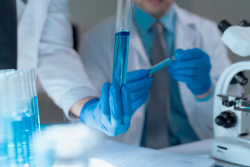 Close up of scientists wearing gloves and holding test tubes with blue liquid, conducting...
