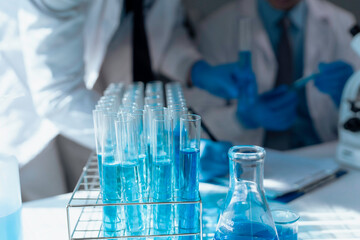 Scientific glassware filled with blue solution during research, laboratory technicians performing analysis in sterile workspace