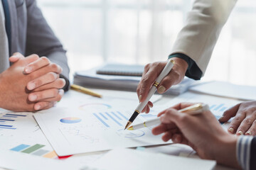 Professional team reviewing financial reports, gesturing toward statistical charts during collaborative corporate strategy session