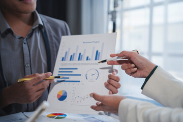 Business team analyzing financial data, using pens to point at charts and graphs, discussing...
