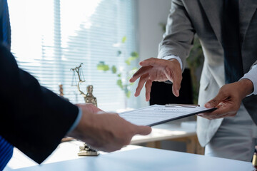 Two lawyers in suits reviewing and exchanging legal documents, discussing contract terms and conditions in a bright office