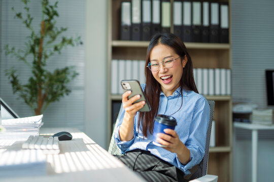 Smiling professional relaxing during workday, scrolling smartphone and sipping coffee at desk