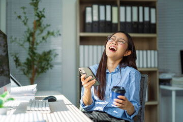 Female professional sipping coffee and scrolling smartphone, laughing while working at modern...