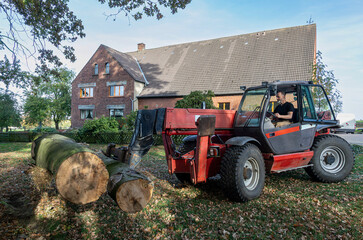 Heavy-duty telehandler moving large tree logs on a farm.