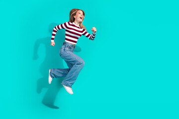 Joyful young woman jumping with excitement over a turquoise background showcasing her vibrant...