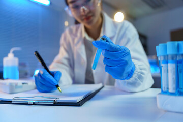 Scientific researcher documenting chemical experiment, wearing protective gear, examining blue solution during laboratory investigation