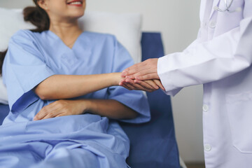 Doctor is holding hand of smiling patient lying in hospital bed, showing empathy and support