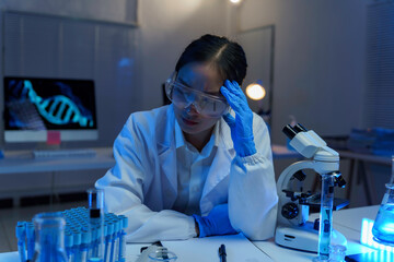 Fatigued asian female researcher experiencing migraine while conducting late night medical study in sterile laboratory setting