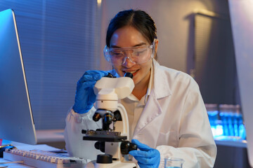 Female scientist examining specimen under microscope, wearing protective gear in high tech research laboratory