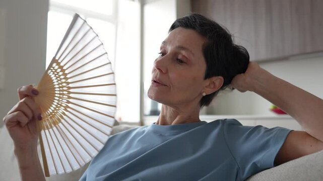 Weary tired stressed woman fanning at home, sweating profusely. No conditioning, oppressive weather, difficulty breath, suffocating, heart pressure, extreme temperatures, struggle with heat at home