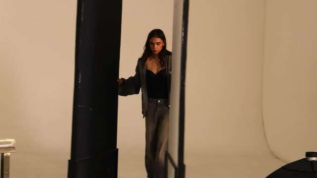 A young female gaffer adjusts foam reflectors in a photo studio, carefully positioning them to control lighting and enhance the scene. She is focused on optimizing the light setup for a professional 